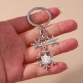 Detail showing silver alloy snowflake charms on a keychain held in hand for size view - Triple Snowflakes