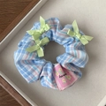 Close-up of blue plaid scrunchie with green bows and floral hand-stitched label - Blue