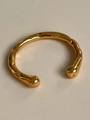 Detalle macro del brazalete abierto bañado en oro 18K con texturas martilladas y puntas esféricas - Dorado