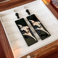 Detalle macro de pendientes rectangulares negros con diseño de orquídea en joyero - Estilo Orquídea de Rectángulo Negro