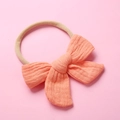 Close-up of peach muslin cotton bow and nude nylon elastic headband for infants - Light Orange