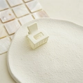 Primo piano di una pinza per capelli quadrata crema opaca su un piatto di ceramica - Bianco