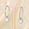 Detalle de pendientes de aro plateados con colgantes de corazón de esmalte blanco - Pendientes de Aro Trenzados con Corazón / Acero y Corazón Blanco