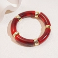 Close-up of red marble acrylic tube beads with gold metal spacers on white stone surface - Dark Red