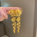 Dettaglio di orecchini pendenti a fiore e foglia dorati tenuti in mano per vedere la misura - Oro (4# Perno in Argento-Eco)