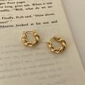 Nahaufnahme von goldenen geflochtenen Creolen auf Vintage-Buchseiten im Shop - Gold / Ohrringpfosten