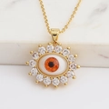 Macro shot of gold evil eye pendant featuring orange center stone and zircon stones - Orange