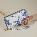 White long wallet with blue butterfly print and dual zippers held by hand - Blue