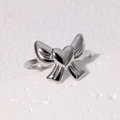 Anello fiocco argento con cuore in acciaio inossidabile, stile minimalista su sfondo bianco - Design con Fiocco e Intarsio a Cuore / Color Acciaio