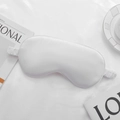 Satin sleep mask in pure white silk finish with elastic headband on soft bedding - White
