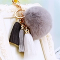 Detail of grey fluffy faux fur pom-pom with black, grey, and white silk tassels on gold ring - Gray