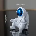 Seated white astronaut ornament with blue visor, measuring 4.5cm by 5.2cm by 4.1cm - No.11 Blue Astronaut / 4.5x5.2x4.1cm