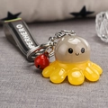 Close-up of octopus keychain with HERO strap, small red bell, and beige acrylic details - Gray