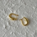 Dettaglio dei orecchini a goccia dorati lucidi su uno sfondo bianco strutturato - Cerchio a Forma di Goccia d'Acqua / Oro