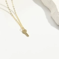 Collana con ciondolo a chiave dorata ed elegante catenina sottile su sfondo di pietra bianca - Chiave