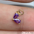 Foto macro de un colgante corazón dorado 6,2x10,6mm con circonitas púrpuras en el dedo - Morado