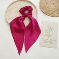 Detail of a rose red satin scrunchie with long ribbons on a white background with props - Rose Red