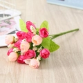 Detailed view of artificial pink rose buds and green leaves on light wood grain surface - Chunxing / Rose Red