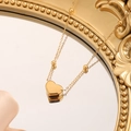 Elegante collar de corazón dorado con cadena de cuentas en un espejo vintage - Dorado