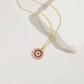 Gold Evil Eye sunburst pendant necklace with blue resin and zircon stones on white stone - Red Evil Eye
