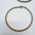 Detailed close-up of golden tennis necklace with black and clear oval zircon stones - White + Black