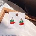 Macro shot of festive red bell earrings with green bows and sparkling zircons - Bell