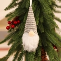 Close-up of a knitted Christmas gnome ornament with white beard on pine branches - Knitted Hanging Grey Style A