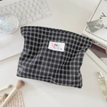 Close-up of black and white plaid makeup bag with logo patch on a desk setting - Black