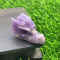 Dragon head carved from natural purple crystal on dark wood base in outdoor setting - Phosphosiderite