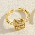 Detalle de anillo cuadrado chapado en oro con circonitas sobre fondo de papel texturizado - Circonita Cuadrada / Dorado