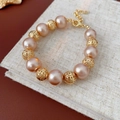 Detail eines Armbands aus rosa Perlen und goldenen Hohlperlen auf beigem Leinen - Armband - Gold