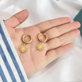 Detailed close-up of golden daisy pendant earrings held by hand on white fabric background - Daisy Shape (DE066)