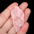 Hand-carved pink crystal leaf charm with detailed veins held in hand for scale - Rose Quartz