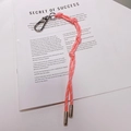 Détail d'un porte-clés en corde tressée rose avec fermoirs métalliques sur un magazine - 8.A05 Lanière Rose