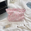 Pink floral quilted cosmetic bag on a bed with makeup brushes and lifestyle items - Flower White Rabbit