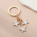 Detail of golden alloy keychain with three white enamel star-shaped pendants on peach surface - White
