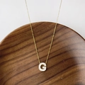 Collier doré en titane avec pendentif lettre G en nacre blanche sur plateau bois - Lettre G