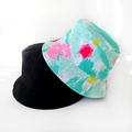 Flat lay of foldable bucket hats in solid black and mint green splatter star print - Colorful Paint Splatter