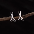 Minimalist silver scissors stud earrings in stainless steel on a dark wood stand - Steel