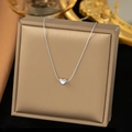 Minimalistische silberne Herzanhänger-Halskette auf einem champagnerfarbenen Display - Mini-Herzhalskette (H463) / Stahlfarben