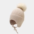 Detail of cable knit earflap hat with large faux fur pompom and woven ties - Beige