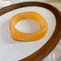 Vista detallada de un brazalete ancho de resina acrílica naranja sobre una bandeja de madera - Brazalete ancho irregular / Pulsera Ámbar