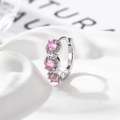 Silberne geometrische Creolen mit drei runden rosa Zirkon-Steinen auf weißem Stoffgrund - Rosa