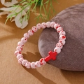 Beaded bracelet with white-red stones and a red cross pendant on a grey pebble - White Red Spotted Red Cross Bracelet