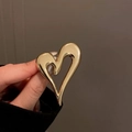 Dettaglio ravvicinato di una spilla a forma di cuore dorata con finitura metallica liscia - Oro