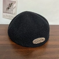 Boina clásica de lana negra para mujer con etiqueta metálica sobre superficie de madera - Negro