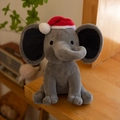 Cute gray plush elephant toy wearing a red mini Christmas hat on a wooden desk - Christmas Grey/Red Christmas Hat