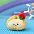 Macro detail view of a soft plush swiss roll charm featuring a cute face and strawberry - Swiss Roll