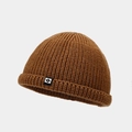 Gros plan sur la maille épaisse et l'étiquette logo noire d'un bonnet en tricot marron - Couleur caramel