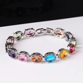 Detail van een zilveren armband met gekleurde ovale edelstenen en kristallen halo - Ovaal